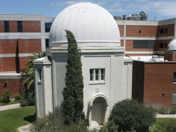 A white observatory dome in the foreground and brick buildings in the background